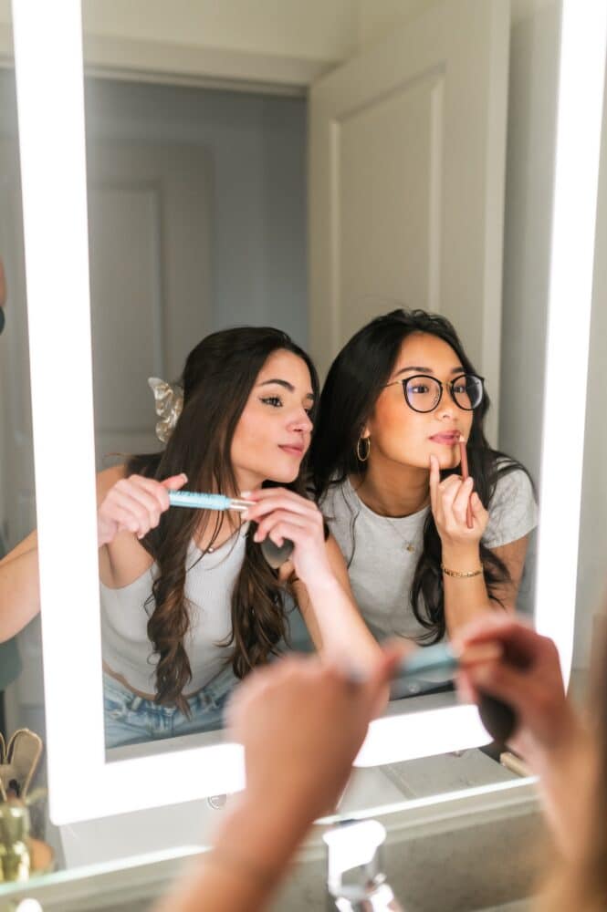 A young woman kneeling on a grassy lawn at night in front of a modern apartment building with large glass windows. She is smiling as a fluffy brown and white dog on a leash leans up to nuzzle her face.