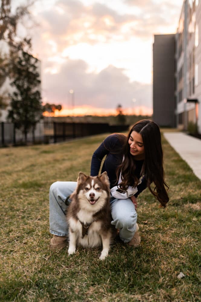 A young man with a bright smile looking at his reflection in a modern, backlit bathroom mirror. He is wearing a patterned short-sleeve shirt and adjusting his hair.